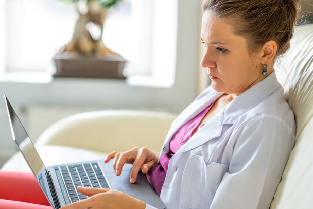Una donna medico con un computer portatile in grembo consulta un paziente in videoconferenza - Foto, immagini