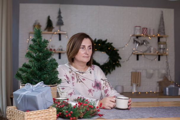 Masada oturan ve Noel süslemeli bir odada çay içen bir kadın. - Fotoğraf, Görsel