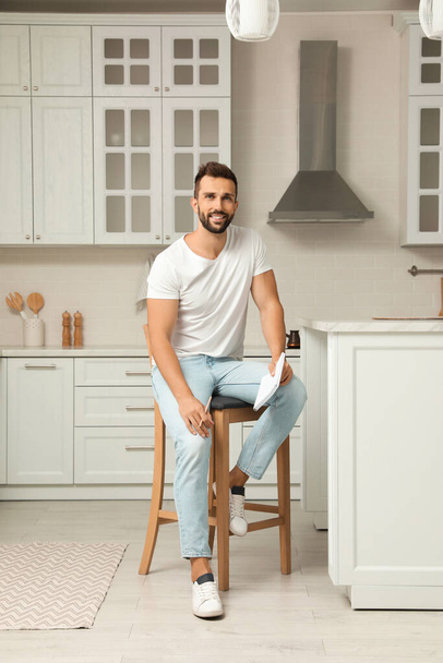 Handsome man with notebook sitting on stool in kitchen - Foto, afbeelding