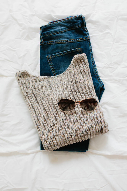 Concepto de moda. Puesta plana: suéter, jeans y gafas de sol sobre un fondo blanco, vista superior. - Foto, Imagen