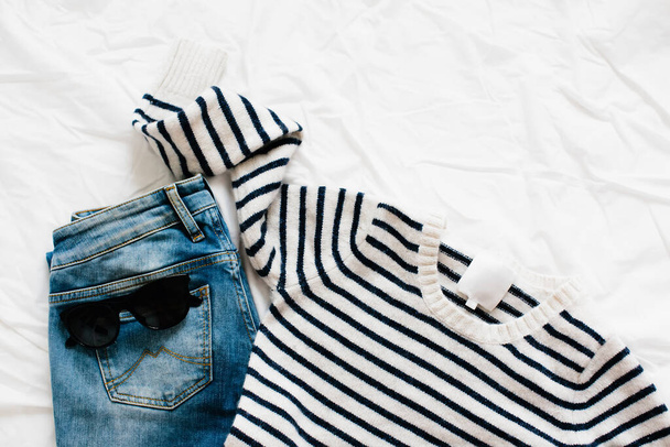 Women's fashion clothes and accessories on a white background, flat lay. Striped sweater and blue jeans. Copy space. - Photo, Image