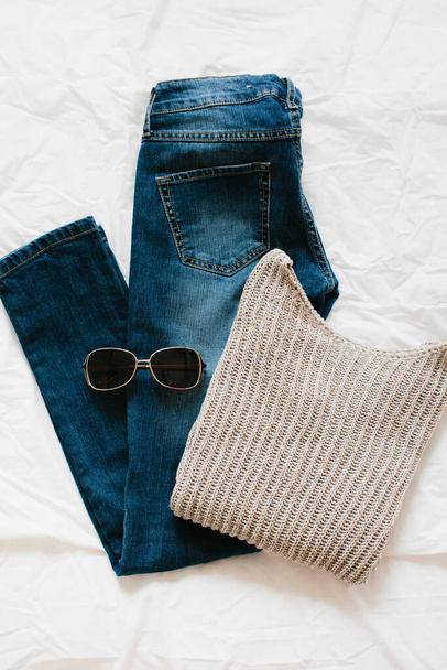 Concepto de moda. Puesta plana: suéter, jeans y gafas de sol sobre un fondo blanco, vista superior. - Foto, imagen