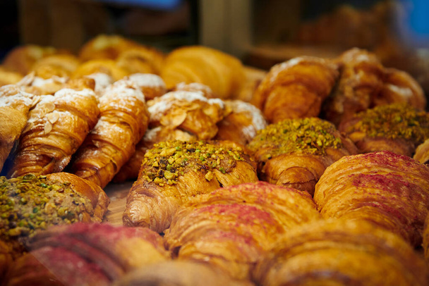 Sok különböző croissant van a cukrászda ablakában. Mandula és pisztáciás croissant. Meleg fény az édességekben. - Fotó, kép