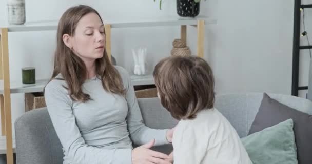 Турботлива мати заспокоює і обіймає маленького чарівного сина, що сидить разом на дивані вдома
 - Кадри, відео