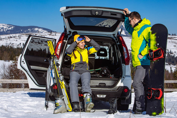 man and woman dressing into ski equipment near suv car. mountains on background - Photo, Image