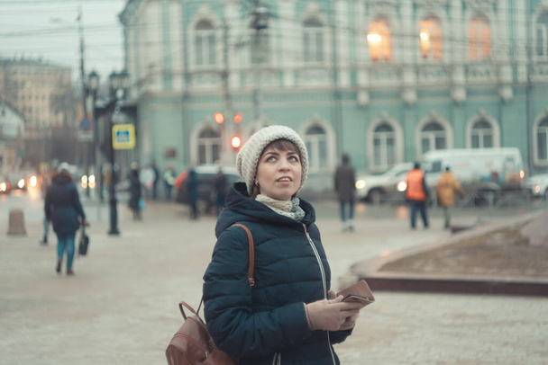 a girl in a winter hat walks around the city, looks at the buildings - 写真・画像