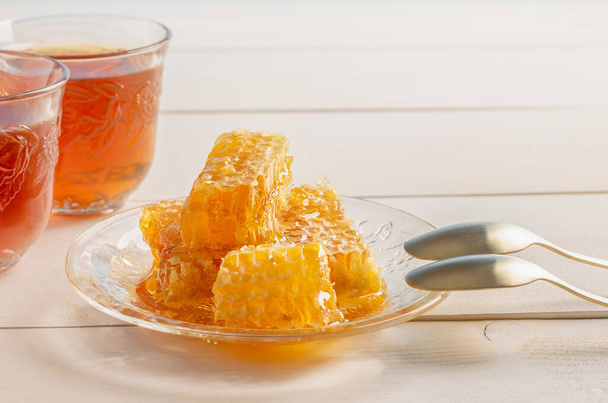 Kousky plástve medu a dva šálky čaje ve skleněných nádobách na dřevěném stole. Kopírovat prostor. - Fotografie, Obrázek