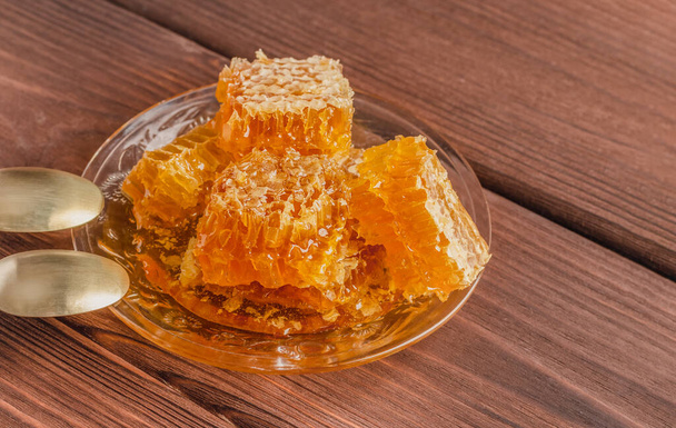 Φρέσκο μέλι σε κηρήθρα σε γυάλινο πιάτο σε ξύλινο τραπέζι. - Φωτογραφία, εικόνα