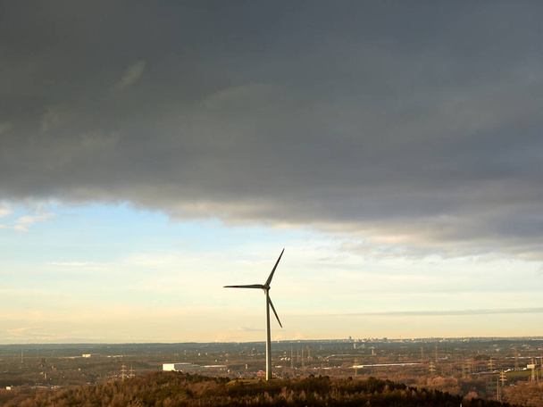 Pojedyncza turbina wiatrowa stojąca na stosie Hoppenbruch w mieście Herten w Niemczech. Nadciągające chmury deszczowe nad Ruhr Metropolis. - Zdjęcie, obraz