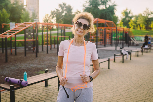 Regular exercise is big part of healthy lifestyle. Happy mature woman relaxing after jumping training. Concept active lifestyle and healthcare in mature age. Senior lady standing with skipping rope. - Photo, Image