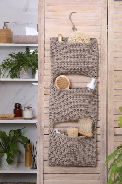 Storage with essentials hanging on wooden folding screen in bathroom. Stylish accessory - Fotó, kép