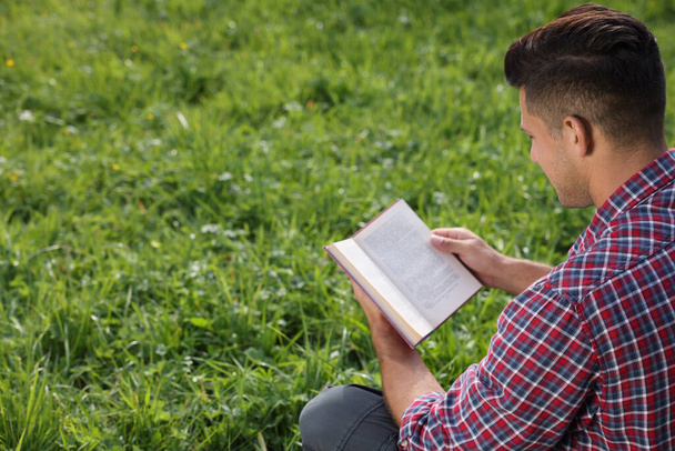 Man reading book on green grass outdoors - 写真・画像