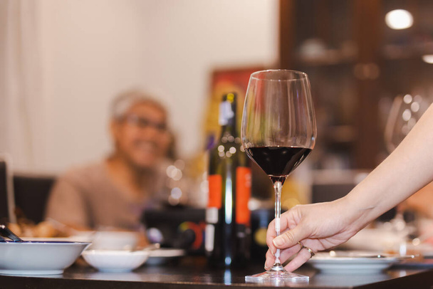 Donna che tiene il vino rosso di vetro sul tavolo da pranzo. - Foto, immagini