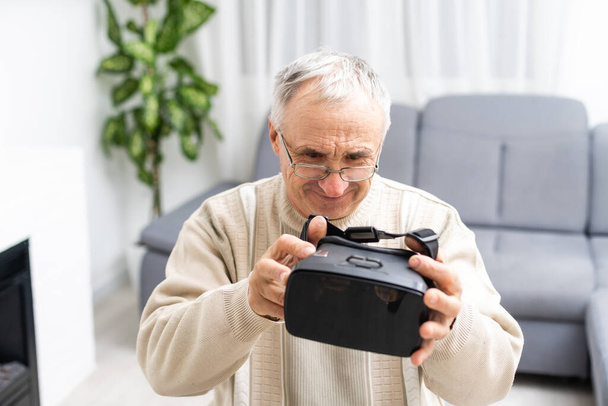 technologie, augmented reality, gaming, entertainment en mensen concept - senior man met virtuele hoofdtelefoon of 3d bril videogame thuis spelen. - Foto, afbeelding