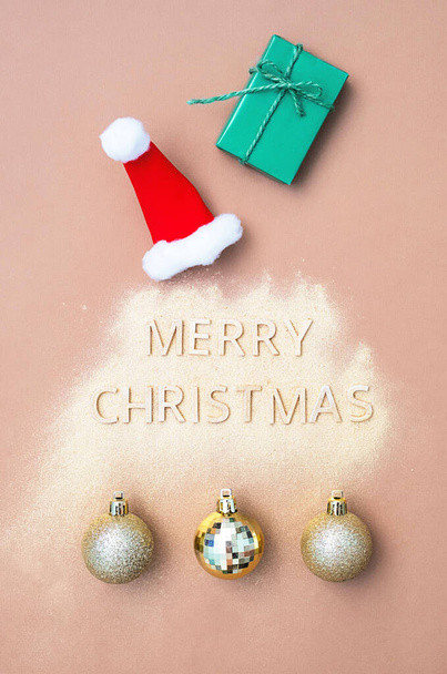 Merry Christmas - words, Santa Claus red hat, green gift box flat lay on neutral background. Poster, invitation or greeting card for Christmas holiday. - Photo, Image