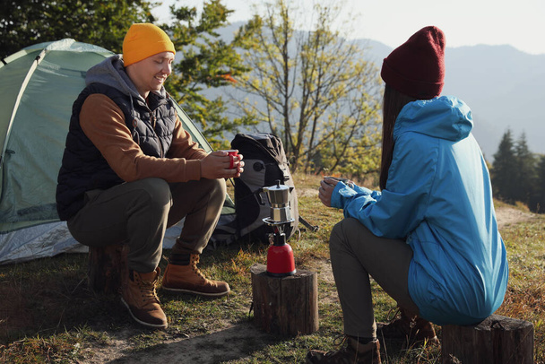 Young couple drinking coffee near camping tents in mountains - Fotoğraf, Görsel