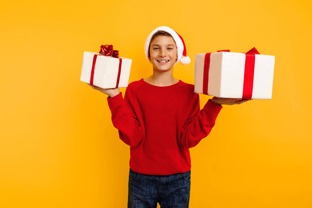 happy young boy in red sweatshirt with gift and santa claus hat. received a christmas present. emotions of joy. christmas concept, new year. on a yellow background. - Foto, immagini