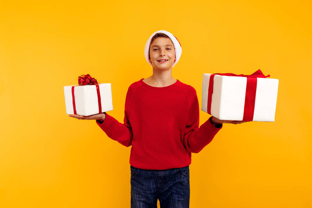handsome young boy in a red sweatshirt with a gift and a santa claus hat. holding a Christmas present. christmas concept, new year, lovers day. - Fotografie, Obrázek