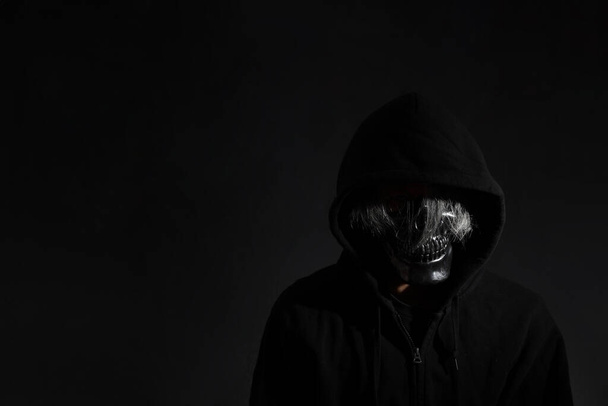Ο άνθρωπος του τρόμου με τη μάσκα του κρανίου στέκεται στο σκοτάδι. - Φωτογραφία, εικόνα