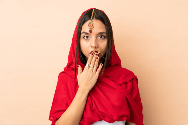 Mujer india joven aislada sobre fondo beige cubriendo la boca con la mano - Foto, Imagen