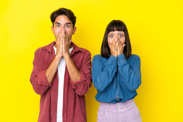 Young mixed race couple isolated on yellow background smiling a lot while covering mouth - Photo, image