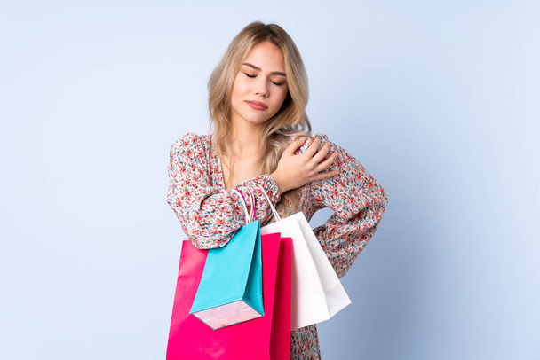 Ragazza russa adolescente con shopping bag isolato su sfondo blu che soffre di dolore a spalla per aver fatto uno sforzo - Foto, immagini