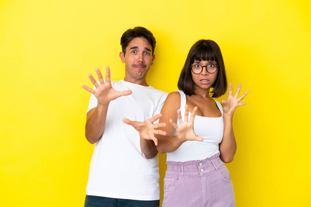 Jeune couple mixte isolé sur fond jaune est un peu nerveux et effrayé étirant les mains à l'avant - Photo, image