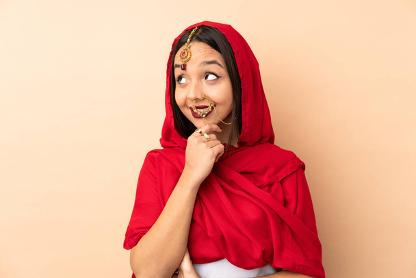 Jeune femme indienne isolée sur fond beige penser une idée tout en levant les yeux - Photo, image
