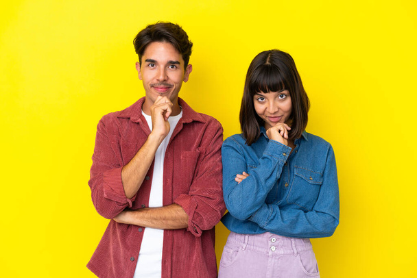 Young mixed race couple isolated on yellow background smiling and looking to the front with confident face - Photo, Image