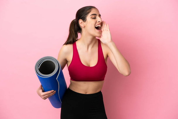 Giovane donna caucasica sport andando a lezioni di yoga, mentre tenendo un tappeto gridando con la bocca spalancata al lato - Foto, immagini