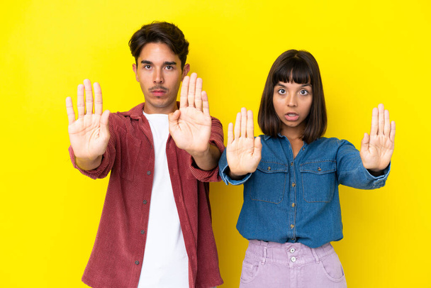 Young mixed race couple isolated on yellow background making stop gesture for disappointed with an opinion - Photo, Image
