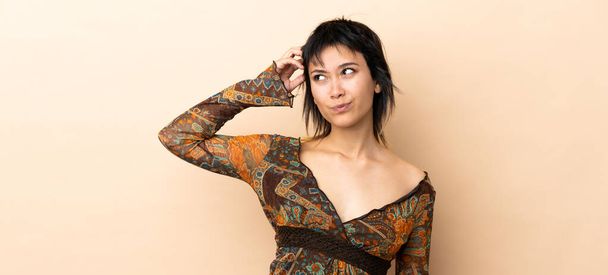 Indian woman isolated on beige background having doubts while scratching head - Foto, imagen