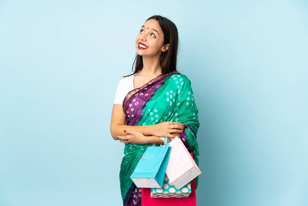 Молодая индийская женщина с сумками смотрит вверх, улыбаясь - Фото, изображение