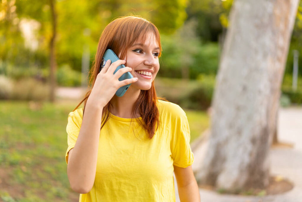 Jonge mooie roodharige vrouw buiten houden van een gesprek met de mobiele telefoon met iemand - Foto, afbeelding