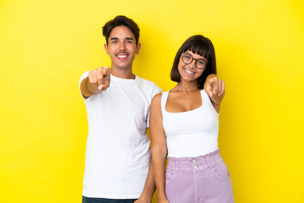 Young mixed race couple isolated on yellow background points finger at you with a confident expression - Photo, Image