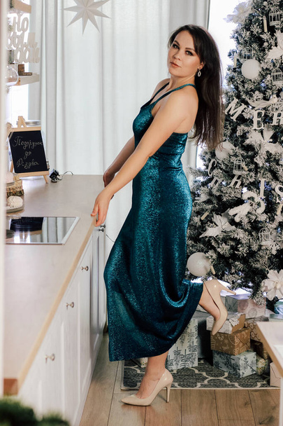 Дівчина з темним волоссям в блискучій елегантній сукні позує в новорічному інтер'єрі
. - Фото, зображення