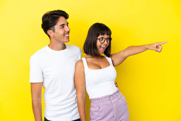 Nuori sekarotuinen pari eristetty keltaisella taustalla esittää idean katsoen hymyillen kohti - Valokuva, kuva