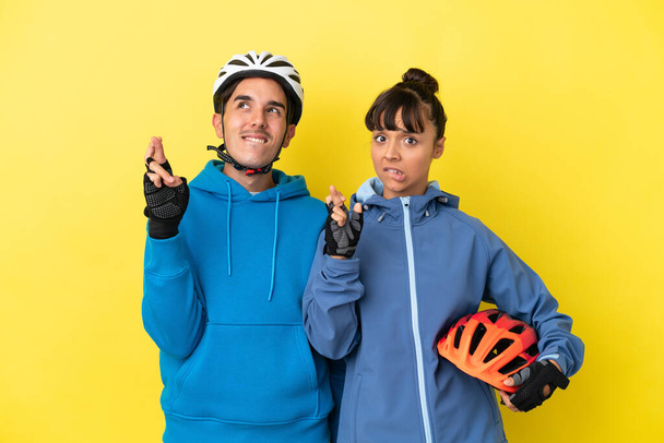 Junges Radlerpaar isoliert auf gelbem Hintergrund mit Daumendrücken und besten Wünschen - Foto, Bild