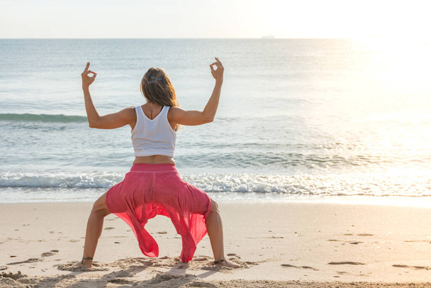 Женщина на пляже делает позу йоги konasana utkata, глядя на море - Фото, изображение