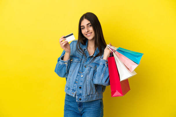 Mavi arka planda izole edilmiş beyaz bir kadın elinde alışveriş çantaları ve bir kredi kartı tutuyor. - Fotoğraf, Görsel