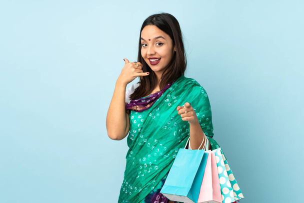 Alışveriş çantalı genç Hintli kadın telefon hareketlerinde ve ön tarafı işaret ederek - Fotoğraf, Görsel