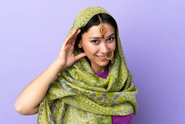 Mor arka planda izole edilmiş Hintli bir kadın bir şey dinlerken elini kulağına koyar. - Fotoğraf, Görsel