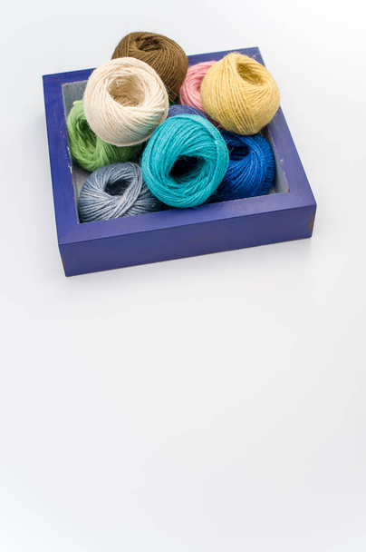 multicolored decorative yarn balls in a wooden box on a white surface - Foto, Bild
