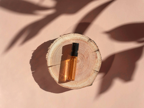 Gölgeli bir ahşap kesim üzerinde kahverengi sıvı ile cam parfüm testi. Üst görünüm - Fotoğraf, Görsel