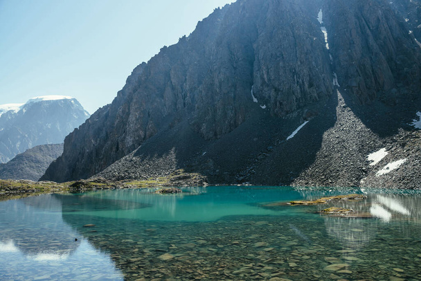 Sunny mountain landscape with azure glacial lake in sunlight. Turquoise clear water of mountain lake and big rock. Beautiful scenery with lake and snow in mountain. Stony bottom in transparent water. - Photo, Image