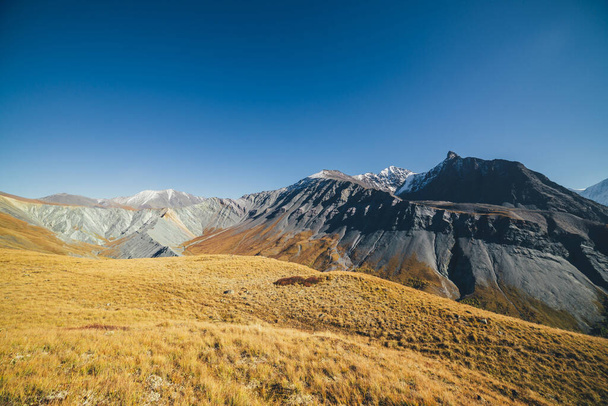 Φοβερό φθινοπωρινό τοπίο με μεγάλα χιονισμένα βουνά και απότομους βράχους. Εντυπωσιακή πολύχρωμη θέα στο βουνό κορυφογραμμή και κίτρινο κοιλάδα το φθινόπωρο. Υπέροχο ορεινό τοπίο σε πορτοκαλί φθινοπωρινά χρώματα. - Φωτογραφία, εικόνα