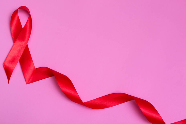Draufsicht auf rosa Hintergrund mit rotem Schleifenkonzept am 1. Dezember zum Internationalen AIDS-Tag Nahaufnahme. - Foto, Bild