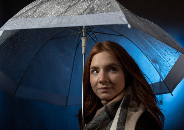 Πορτρέτο του όμορφη κόκκινα μαλλιά κορίτσι με μπλε μάτια στέκεται κάτω από διαφανή ομπρέλα τη νύχτα - Φωτογραφία, εικόνα