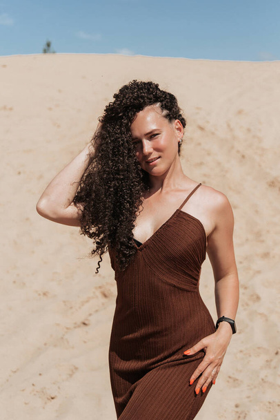 Dark brunette with voluminous curly hair among the Sands in a sand dune in a flying dress. - 写真・画像