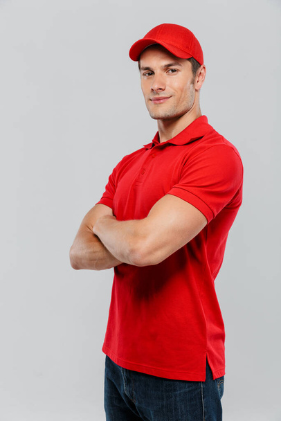Young delivery man wearing uniform smiling while posing with arms crossed isolated over white wall - Fotoğraf, Görsel